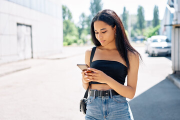 Beautiful black woman looking at her cell phone walking in the city