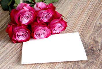 A bouquet of roses with a white leaf for writing on a wooden background.