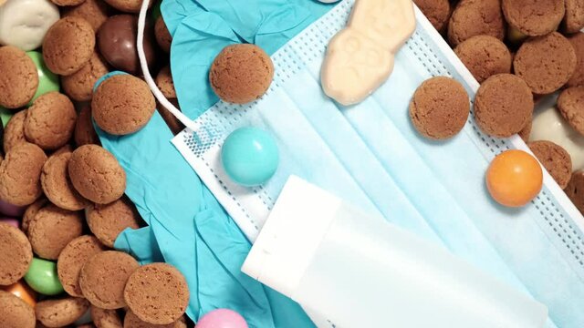 Overhead shot of Dutch holiday Sinterklaas Saint Nicholas day during covid-19 pandemic in the Netherlands with kruidnoten cookies, traditional sweets and medical protective equipment. Rotating