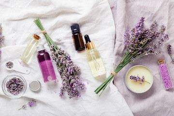 Lavender oils, serum liquids butter parfumes, lavender flowers on white fabric. Set skincare spa...