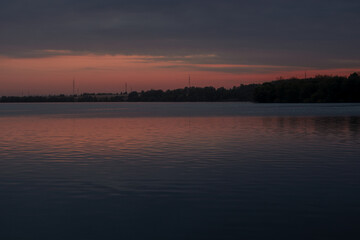 The landscape of the lake shore in Russia against the background of pink twilight, sunset. Large reservoir.