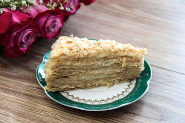 Layered cake with custard cream on the background of a bouquet of flowers.