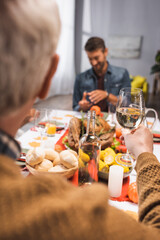 selective focus of senior man holding glass of white wine during thanksgiving dinner with family