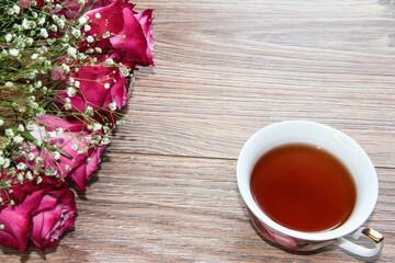 Naklejka na ściany i meble A Cup of tea with roses on a wooden background.