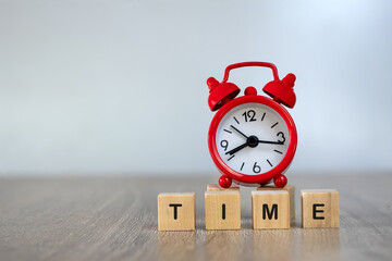 A wooden block with the word time and a red alarm clock placed behind the concept of recognizing the importance of time. Determination of the exact time There is an area for entering text.