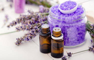Obraz na płótnie Canvas Lavender essential oils and violet sea salt, lavender flowers. Lavender bath products Aromatherapy treatment on white wooden background. Skincare spa beauty bath cosmetic products relax aromatherapy.