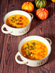 Two bowls of homemade pumpkin soup, decorated with pumpkin seeds and drops of pumpkin oil, on brown background