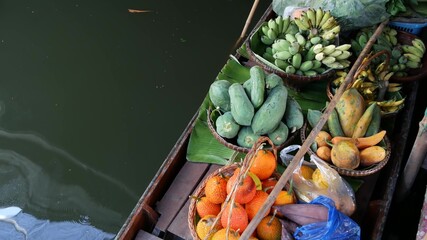 Iconic asian Lat Mayom floating market. Khlong river canal, long-tail boat with tropical exotic colorful fruits, organic locally grown vegetables. Top view of harvest and street food in wooden canoe