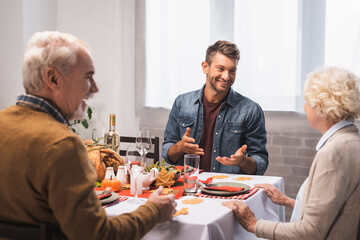 excited man gesturing while talking to senior parents during thanksgiving dinner