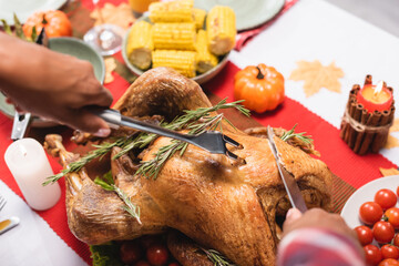 Cropped view of african american woman cutting turkey near candles during thanksgiving celebration