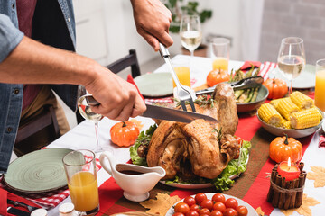 Cropped view of man cutting turkey near thanksgiving decorations on table