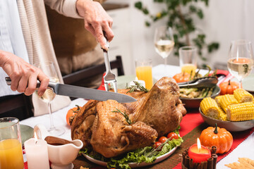Cropped view of senior woman cutting turkey on table during thanksgiving celebration