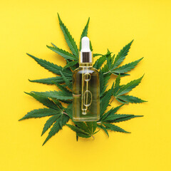 Hemp oil serum in glass dropper bottle on cannabis leaves. Cannabis leaf with skincare cosmetic product CBD oil on yellow background