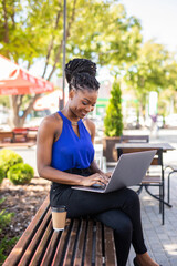 Young african woman in park. Beautiful woman sitting on bench using laptop.