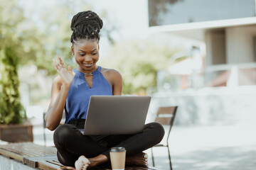 Beautiful young african woman working on laptop computer have video call conversation sitting on a bench outdoors