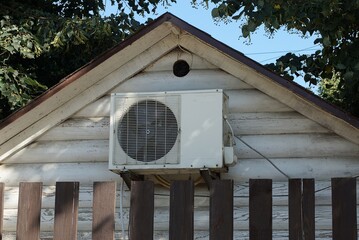 one gray metal air conditioner on a wooden attic wall behind a brown fence outside