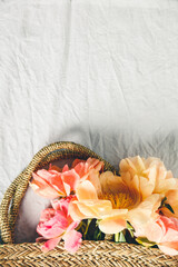 Flat-lay of Beautiful peony flowers in straw bag over grey linen table cloth background