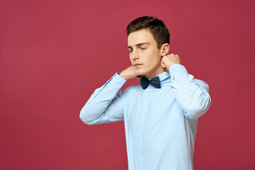 guy straightens his shirt collar and a bow tie around his neck Red background