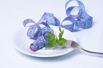 Diet and weight loss concept. White plate and blue measuring tape with green parsley leaves wound...