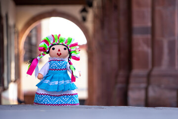 Muñeca de trapo artesanal tradicional con fondo de arco arquitectónico y columnas.