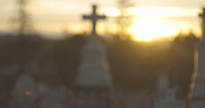 Defocused footage of a Cemetery at Sunset, grave stones and crosses from 1800-1900s visible in the background. Insects flying around in the warm air. Rest in peace.