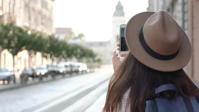 girl traveler in a mask walks through the old European city. Young woman in a hat on vacation takes pictures by smartphone