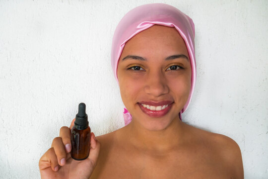 Woman with a pink scarf holding cosmetic oil for facial skin care