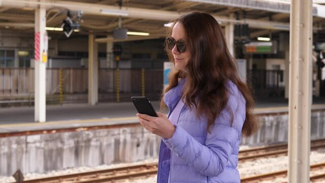 Tourist woman using mobile application, check route and schedule of Japanese rapid transit trains. Lady stand with smartphone at station platform, portrait shot