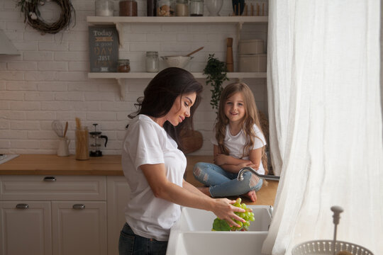 Happy Loving Family Preparing Food Together. Smiling Mom And Child Daughter Girl Washing Fruits And Vegetables And Having Fun In The Kitchen. Healthy Food. Little Helper In Scandinavian-style Interior