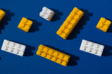 Pattern of colored plastic blocks of the children's designer white and yellow on a blue background. Child development concept, logic, thinking and fine motor skills