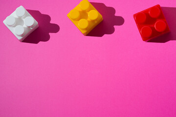 Pattern of multicolored plastic blocks of children's constructor on a pink background with copy space