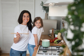 Happy loving family preparing dinner together. Smiling Mom and child daughter girl cooking and having fun in the kitchen. Homemade healthy food. Little helper in the white Scandinavian-style interior.