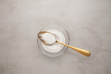 Collagen powder in glass bowl and golden spoon on light stone background. Extra protein intake. Natural beauty and health supplement for skin, bones. Flat lay, top view, copy space