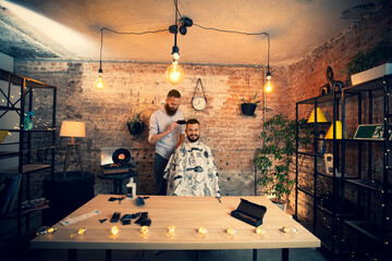 Good looking man visiting barber shop. The barber cuts his hair and trims his beard.