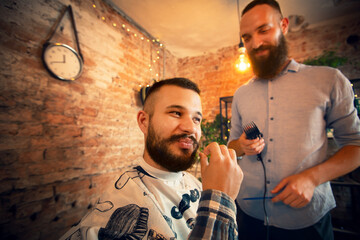 Good looking man visiting barber shop. The barber cuts his hair and trims his beard.