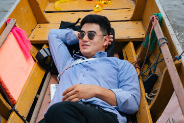 Fototapeta na wymiar Business man wear sunglasses sleep on wooden boat in Bangkok.