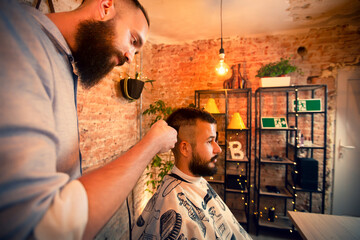 Good looking man visiting barber shop. The barber cuts his hair and trims his beard.