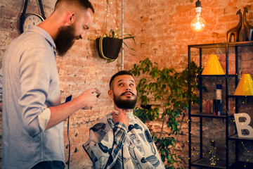 Good looking man visiting barber shop. The barber cuts his hair and trims his beard.