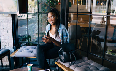 Cheerful woman browsing smartphone and smiling at camera