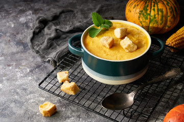 Traditional pumpkin soup puree with crackers, cream and seeds in a bowl, on a dark background