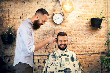 Good looking man visiting barber shop. The barber cuts his hair and trims his beard.