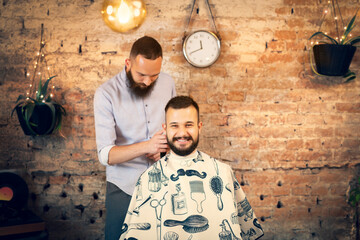 Good looking man visiting barber shop. The barber cuts his hair and trims his beard.