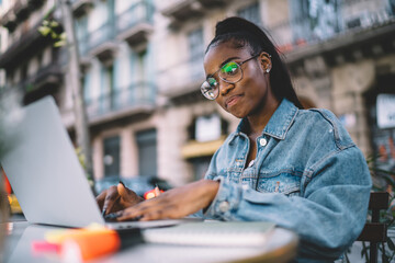 Fototapeta premium Thoughtful young ethnic lady using laptop in outdoor cafe