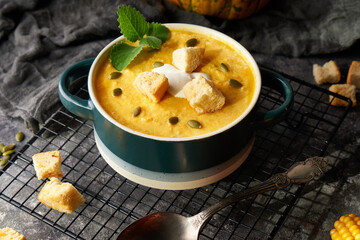 Traditional pumpkin soup puree with crackers, cream and seeds in a bowl, on a dark background