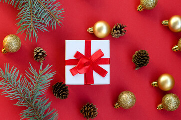 Fototapeta na wymiar holidays, winter and celebration concept - Christmas composition. gift box, pine cones, christmas tree, golden balls on red background. Flat lay, top view.