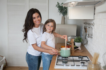 Happy loving family preparing dinner together. Smiling Mom and child daughter girl cooking and having fun in the kitchen. Homemade healthy food. Little helper in the white Scandinavian-style interior.
