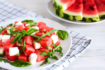 Fresh delicious juicy salad with watermelon, feta cheese, arugula and basil leaves on white plate. Healthy food concept. Close-up. Side view.