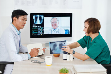Fototapeta na wymiar Radiologist showing lungs x-ray to colleague at online meeting with experienced oncologist
