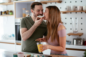 Young couple making breakfast at home. Loving couple eating sandwich in kitchen.