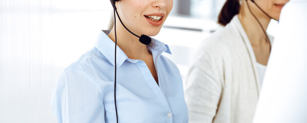Female call operator is using computer and headset for consulting clients online, close-up. Group of diverse people working as customer service occupation